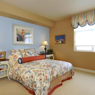 A cozy bedroom with floral bedding and decorative wall art, complemented by a nightstand and table lamp.