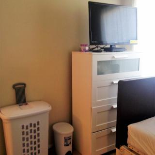 A bedroom corner featuring a dresser with a TV on top, accompanied by a laundry basket and trash can.