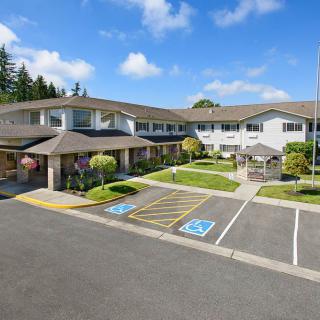 A large residential or commercial building with a parking lot and landscaped grounds under a partly cloudy sky.
