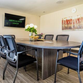 A modern conference room with a large meeting table and chairs, decorated with flowers and wall artwork.