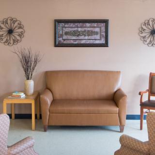 A cozy waiting room with a comfortable sofa and chairs, adorned with decorative wall art and a vase on a side table.