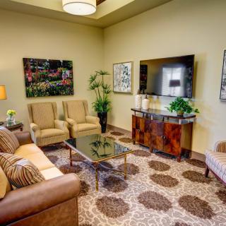 A cozy living room featuring a sofa, armchairs, coffee table, and wall-mounted TV, accented with plants and artwork.