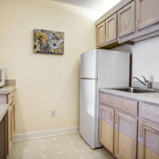 A small kitchen area with wooden cabinets, a refrigerator, and a countertop sink.