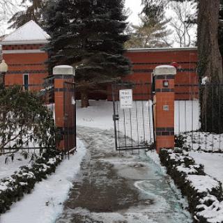 A snow-covered pathway leading to a gated entrance in a winter landscape.