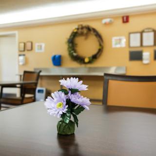 A cozy dining area featuring a small vase of flowers on a table, complemented by a decorative wreath on the wall.