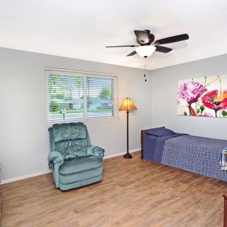 A cozy bedroom featuring an armchair, single bed, and floral wall art, with natural light coming in through the window.