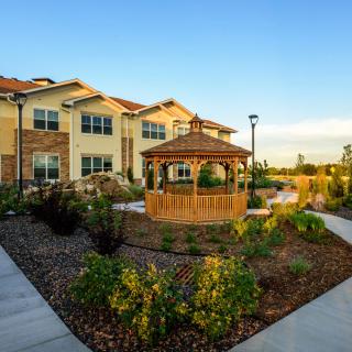 A scenic view of a landscaped garden with a gazebo in front of a residential building.