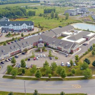 Aerial view of a complex with multiple buildings, a parking lot, and surrounding greenery.