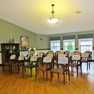 An empty room with arranged chairs, featuring large windows and a central light fixture.