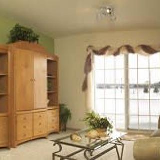A cozy living room featuring a large window with curtains, a wooden cabinet, and a glass coffee table.