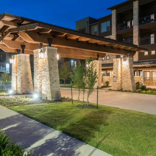 An illuminated building entrance with stone pillars and well-maintained landscaping at night.