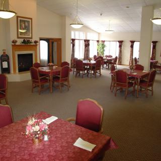 A spacious dining room with multiple round tables and chairs, featuring a cozy fireplace and large windows.