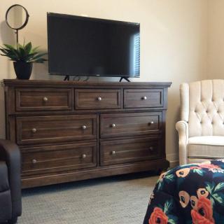 A cozy bedroom setup with a wooden dresser, television, and an upholstered chair.