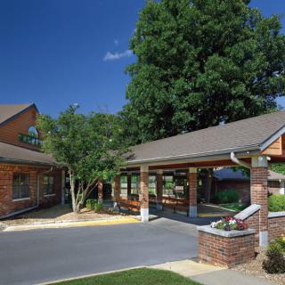 A brick building with a covered entrance surrounded by trees and landscaping.