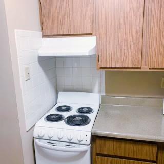 A compact kitchen area featuring a stove and oven next to a countertop and wooden cabinets.