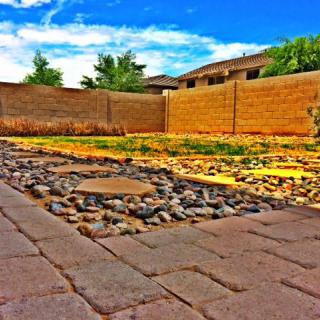 A serene backyard featuring a stone path and a brick wall, set under a clear blue sky in a residential area.