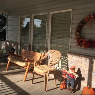 A cozy porch decorated for autumn with chairs, a wreath, and scarecrow figurines.
