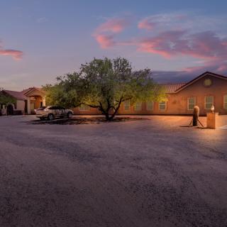 A serene parking lot at sunset with a large tree and a building in the background.