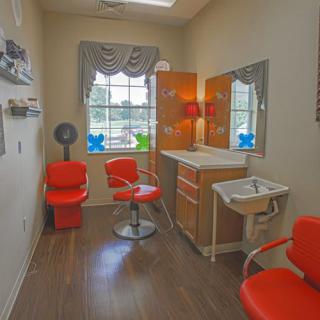A cozy beauty salon interior with red chairs, a mirror, and a hair drying station.