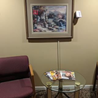 A cozy waiting area featuring a framed picture on the wall, a glass table with magazines, and two chairs.