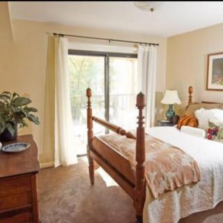 A cozy bedroom with a wooden bed, natural light streaming in through a sliding door, and tasteful decor.