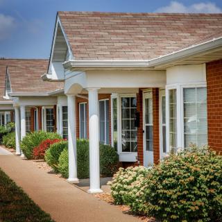 A row of suburban houses with brick exteriors, featuring columns and manicured landscaping along a paved pathway.