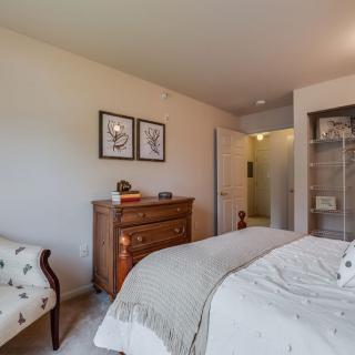 A cozy bedroom featuring a bed, dresser, and chair, with decorative artwork on the walls.