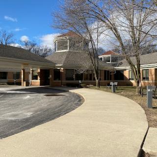 A view of a serene building with a curved pathway, surrounded by trees under a clear blue sky.