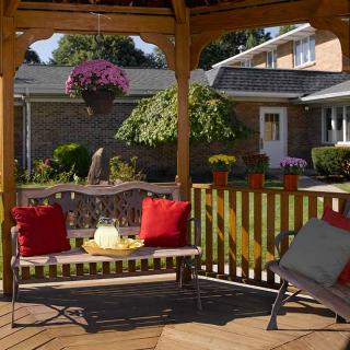 A cozy backyard gazebo with wooden seating, adorned with red cushions and surrounded by a lush garden.