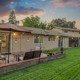 A cozy backyard with a well-maintained lawn and a patio featuring outdoor seating, surrounded by trees at sunset.
