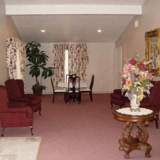 A traditionally decorated living room with plush red chairs, a small dining area, and a floral centerpiece on a wooden table.