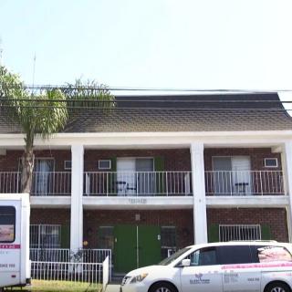 A two-story building with balconies and parked vehicles in front.