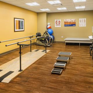 A well-equipped physical therapy room with exercise equipment and parallel bars.