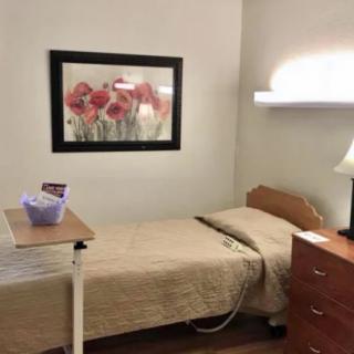 Simple bedroom with single bed, artwork, and bedside furniture.
