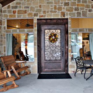 A welcoming entrance featuring a beautifully designed door with a decorative wreath, surrounded by a stone exterior and inviting porch seating.