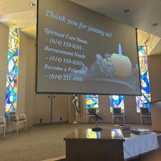 A thank you message displayed on a screen inside a church, featuring colorful stained glass windows.