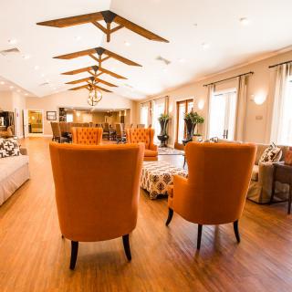A spacious and well-lit lounge area with modern decor, featuring orange chairs and wooden flooring.