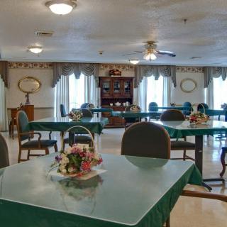 A well-lit dining room with green-covered tables and neatly arranged chairs.
