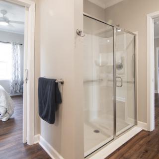 A stylish modern bathroom featuring a glass shower, towel rack, and warm wood flooring.