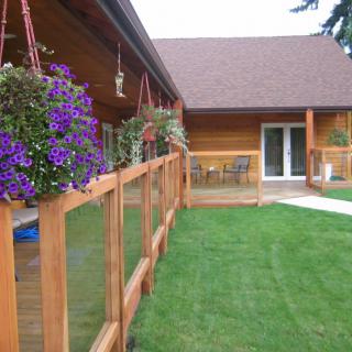 A cozy wooden house with a porch adorned with hanging flowers, overlooking a well-kept lawn and patio area.