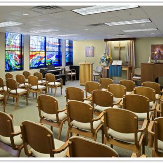 A small chapel with rows of chairs, stained glass windows, and an altar at the front.