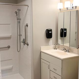 A modern and minimalist bathroom featuring a walk-in shower, sink with mirror, and bright lighting.