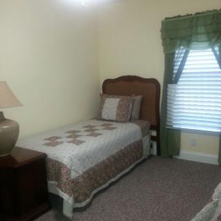 A cozy bedroom with a single bed and decorative quilt near a window with green curtains.