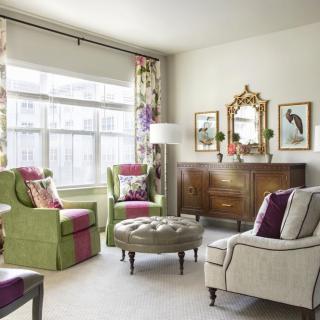 A cozy and elegantly decorated living room featuring colorful armchairs, a tufted ottoman, and wall art.