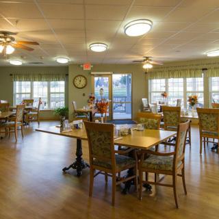 A spacious dining area with multiple tables and chairs, well-lit by overhead lights and natural light from the windows.