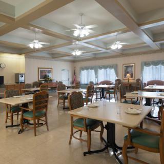 A spacious dining area with neatly arranged tables and chairs, illuminated by ceiling fans.
