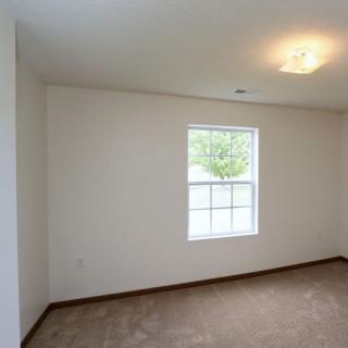 A bright, empty room with white walls, a large window, and a carpeted floor.
