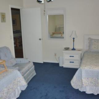 A cozy bedroom featuring twin beds, a chair, and a nightstand with a lamp on a blue carpet.