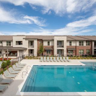 A modern apartment complex featuring an outdoor swimming pool under a clear blue sky.