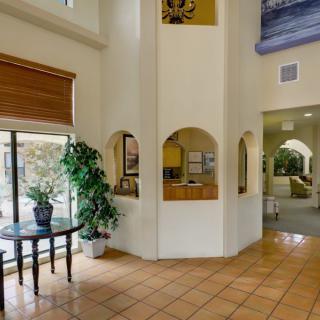 A hotel lobby with tiled flooring, potted plants, and a reception desk.